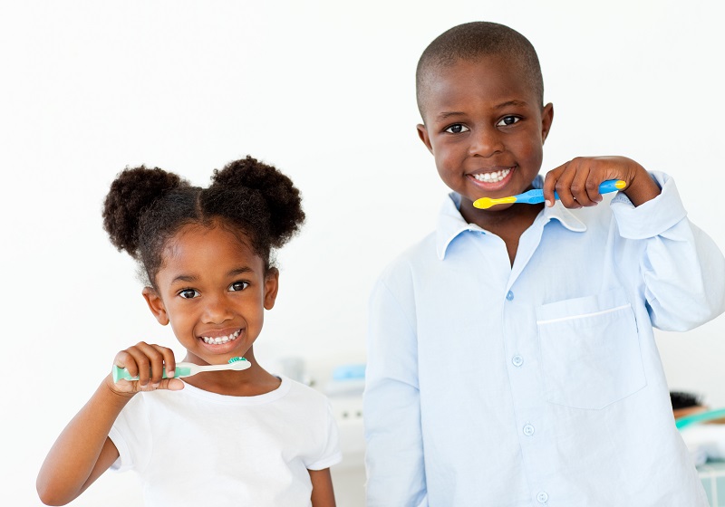 Two childhood siblings smiling and holding toothbrushes with toothpaste up to their mouths