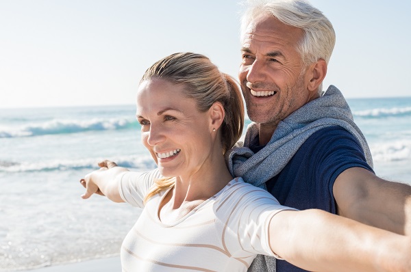 Couple on the beach smiling with implant-supported dentures from Rochester NY