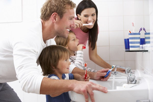 A family of four brushing their teeth in front of the bathroom mirror