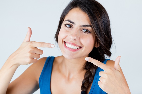 Young woman smiling and pointing at her flawless teeth after porcelain veneer placement