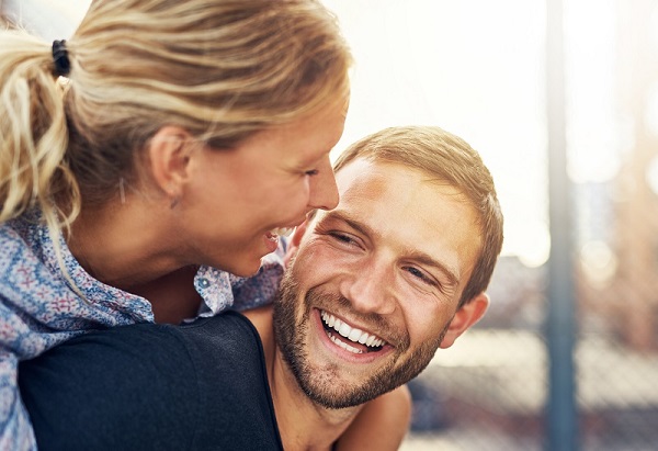 Young blonde couple with the woman looking at the man and the man smiling with whitened teeth