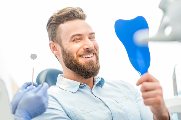 Man smiling and looking at his dental results with a handheld mirror at the dentist's office