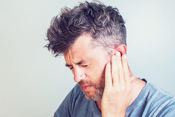 Middle aged man holding his hand up to his TMJ joint and wincing in pain